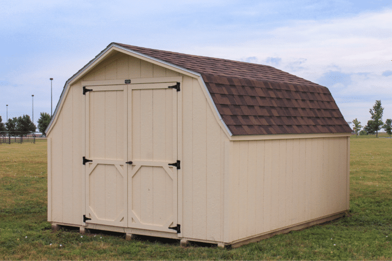 16x48 Sheds Featured Image - Beige barn style shed with double doors and brown shingled roof on grassy field beneath cloudy sky