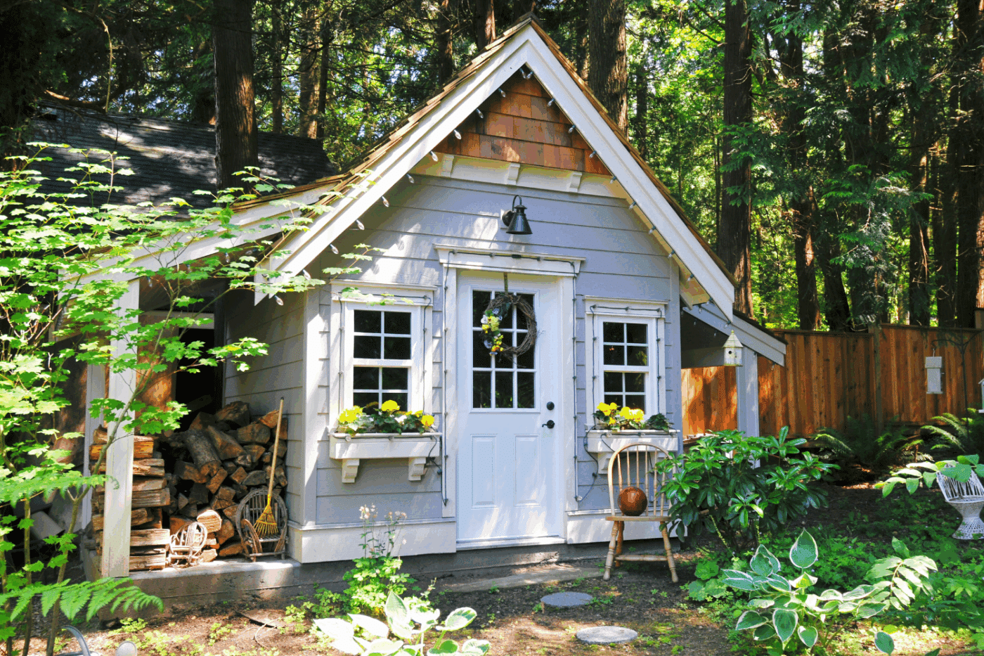 lightly grey shed with shaker roofing shingles and a white door sounded with plants